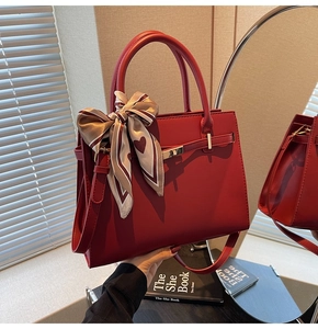 Detail of red leather trapezoid handbag with decorative heart scarf and gold buckle
