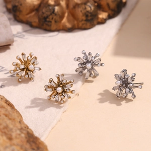 Radial 18K gold starburst earrings with white pearls and baguette zirconias on stone background