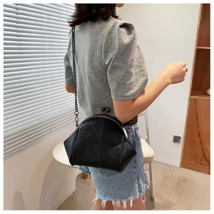 Close-up of black retro shell-shaped chain bag with vintage kiss-lock on female model
