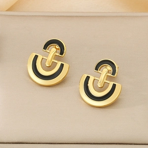 Close-up of golden stainless steel D-shaped earrings with black enamel on beige stand