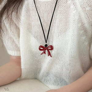 Close-up of a vibrant red bow pendant on a black cord necklace worn by a model