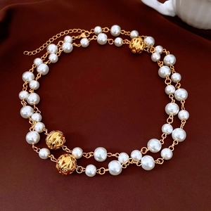 Detail of double-layered pearl necklace with hollow gold beads on red silk background
