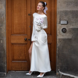 Detail of white satin evening dress featuring a high slit and elegant long sleeves