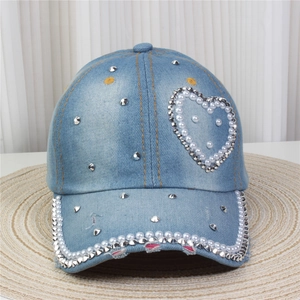 Détail d'une casquette en jean bleu clair ornée d'un cœur en perles et de clous argentés