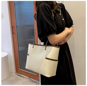 Detail of cream tote bag with brown trim and metal chain strap shown from a side view