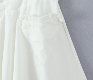 Detail of white dress featuring a heart-shaped pocket with ruffled edges and button detail