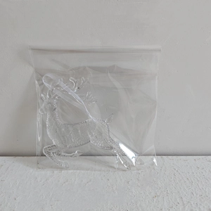 Close-up of a clear acrylic reindeer Christmas ornament in packaging with hanging ribbon