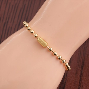 Detail of a gold beaded bracelet featuring a rectangular metal tube charm on a wrist