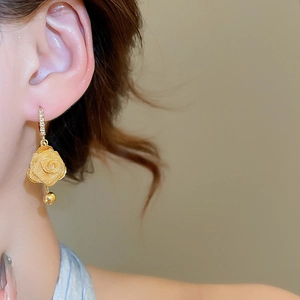 Macro side view of elegant golden rose drop earrings with sparkling diamond studs on model