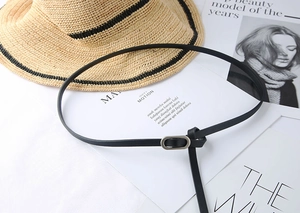 Detail of a slim black leather belt with an oval metal buckle on a minimalist magazine background