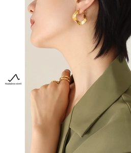 Close-up of golden wavy stainless steel earrings and rings on a model's hand and ear