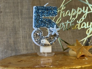 Macro detail of ocean-themed number 5 candle with blue glitter, starfish, and shells