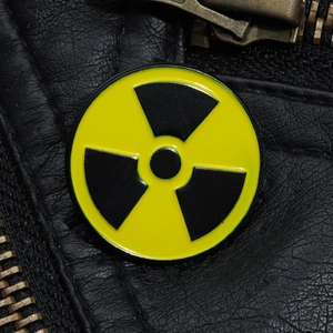 Macro shot of circular yellow and black radioactive symbol enamel pin on black leather jacket