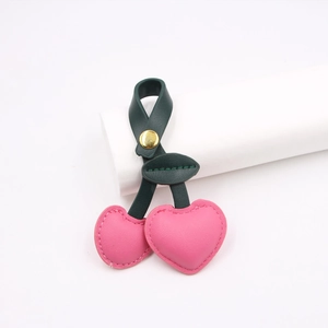Detail of pink leather cherry charm with deep green leaves and gold snap button
