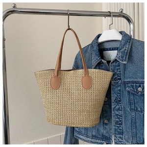 Detail of hand-woven straw bucket bag featuring brown leather handles and natural texture
