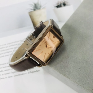 Detail of rectangular rose gold watch with brown leather strap on elegant textured surface