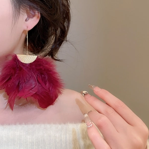 Detailed view of oversized burgundy feather tassel earrings with textured gold metallic top