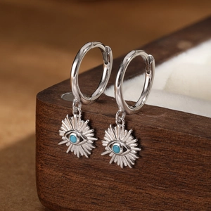 Macro shot of silver evil eye hoop earrings with blue sunburst pendants on wood