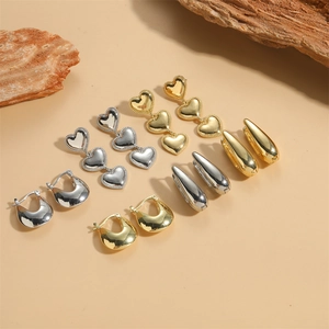 Chic gold and silver U-shaped hoop earrings with heart charms on wooden display