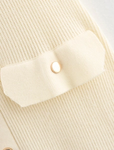 Détail de la texture tricotée crème avec motif côtelé et bouton en métal doré sur la poche