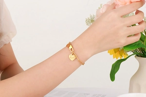 Detail of a gold titanium bracelet featuring heart-shaped Love pendant on a wrist