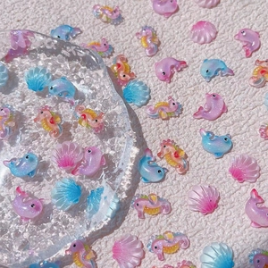 Sparkling resin ocean nail charms featuring glitter dolphins and seashells in pastel gradients