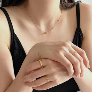 Close-up of minimalist gold beaded necklace and twisted rope rings on model