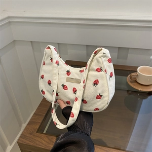 White corduroy strawberry underarm bag with a shoulder strap in a cafe setting