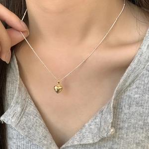 Close-up of minimalist silver bead chain with polished 3D gold heart pendant on neck