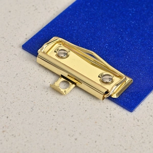Close-up of golden metal clip on blue glitter acrylic clipboard with a retractable hook