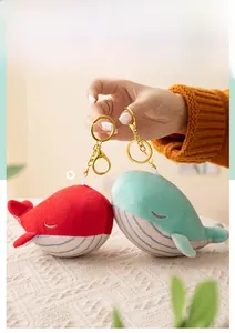 Close-up of cute plush whale pendants with blue stripes and gold keychains in hand