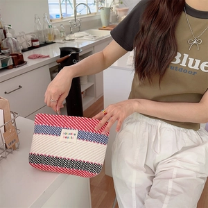 Detail of colorful striped woven toiletry bag held by model in a modern kitchen