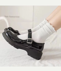 Nahaufnahme schwarzer Lackleder-Mary-Janes mit weißen Socken mit Rüschensaum