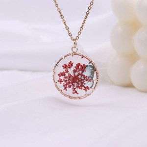 Bohemian gold necklace featuring a round glass pendant with dried flowers and a butterfly