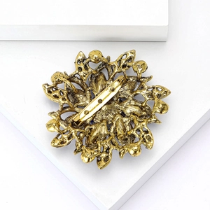 Close-up of elegant gold flower brooch with intricate metal leaf detailing and crystal gems