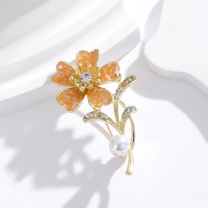 Detail of elegant orange flower brooch with gold plating, sparkling crystals and white pearl