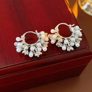 Detailed macro view of silver pearl and rhinestone U-shaped earrings on a wooden box