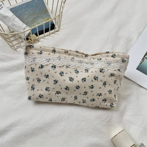 Detailed view of floral makeup bag with lace trim and zipper on a white fabric background