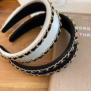 Detail of padded fabric headbands with gold metal chain and woven ribbon on wooden surface