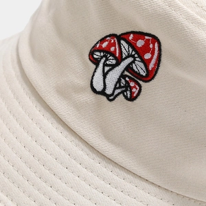 Gros plan d'une broderie de champignon rouge sur un bob en toile beige aux points détaillés
