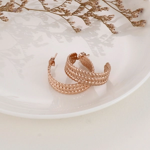 Detail view of rose gold C-shaped twisted rope hoop earrings on a ceramic dish