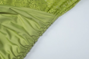 Detailed close-up of light green lace and silk fabric stitching with pleated texture