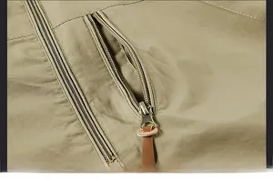 Detail einer khakifarbenen Jacke mit schräger Reißverschlusstasche und Leder-Zuglasche