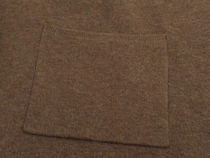 Detail of the brown knit poncho showing a structured ribbed pocket and soft wool texture