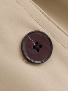 Detailed close-up of dark brown four-hole button on beige twill trench coat fabric