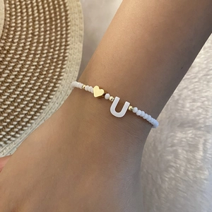 Detail of white beaded bracelet featuring a gold heart and letter U shell pendant charm