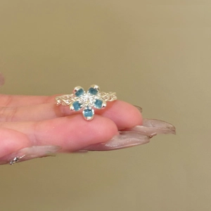 Detail view of a silver woven ring featuring a blue five-petal flower and diamond core