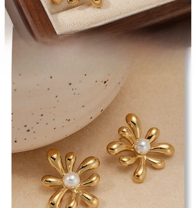 Detail of gold floral earrings with pearls displayed on wooden box and ceramic plate