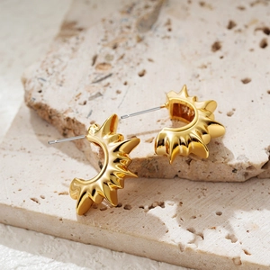 Detail shot of 18K gold sunburst C-shaped earrings on a natural beige stone pedestal