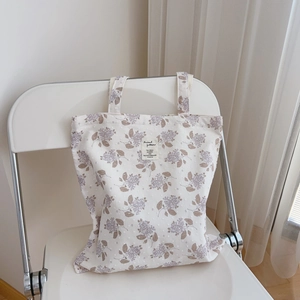 Detail of floral cotton tote bag featuring purple flower patterns and a woven logo label